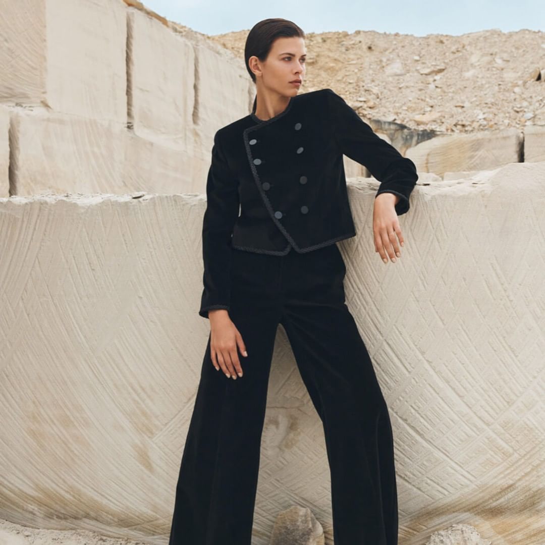Fashionable adult woman in a black velvet blazer and wide-leg pants poses in a quarry, showcasing an elegant and modern style.
