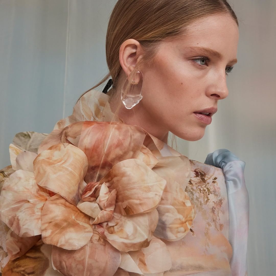 Elegant woman in floral dress and sculptural earrings posing in a softly lit studio environment for a fashion or beauty editorial.
