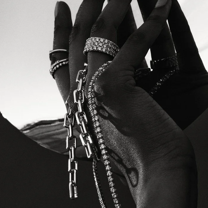 Monochrome close-up of hands adorned with multiple diamond rings and silver link chains by 3 Deep.