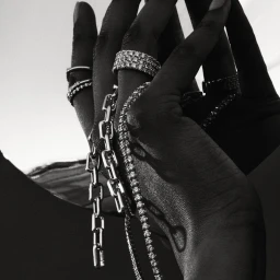 Monochrome close-up of hands adorned with multiple diamond rings and silver link chains by 3 Deep.