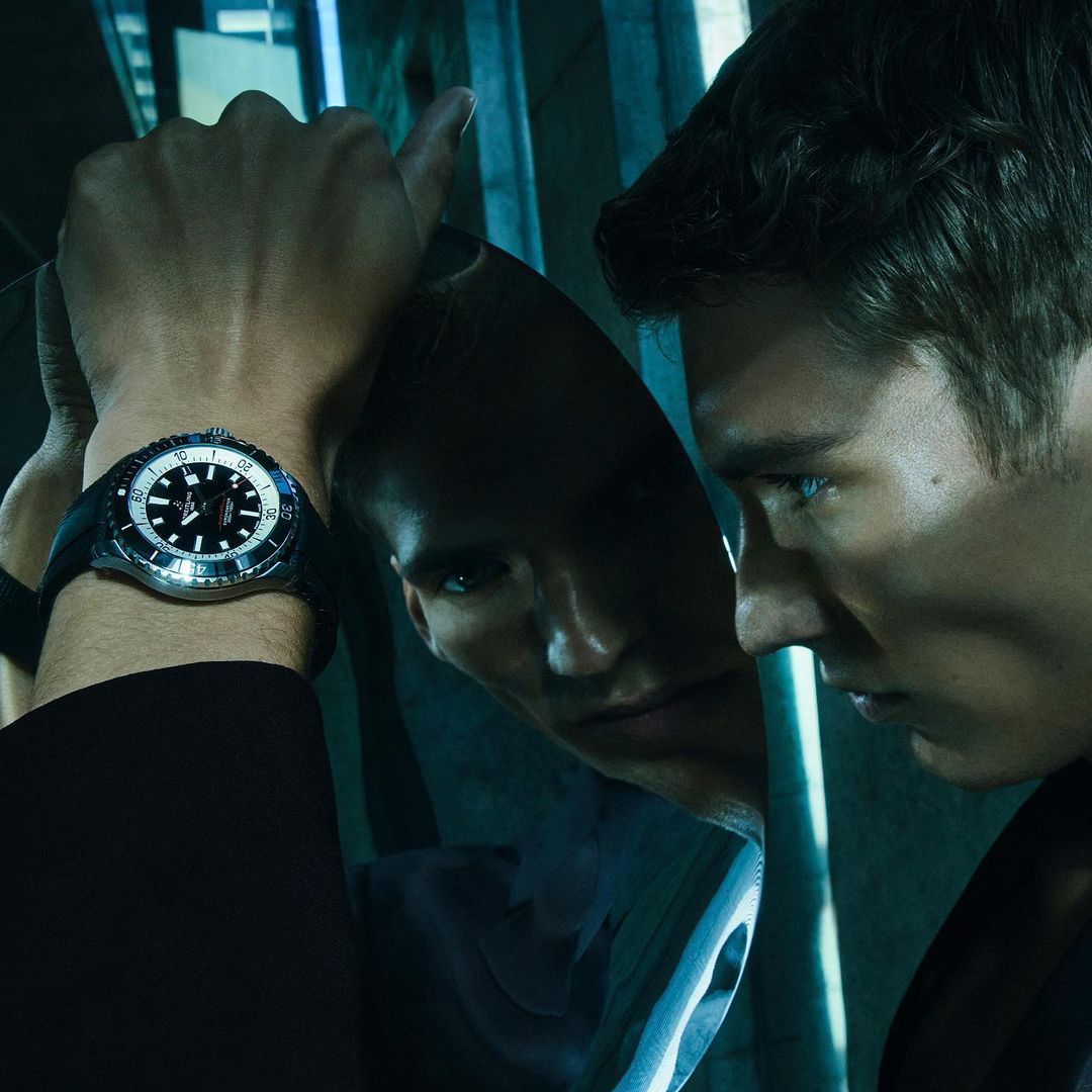 Close-up of a man in a suit looking in a reflective surface, focusing on the wristwatch he's wearing, reflecting in cool tones.