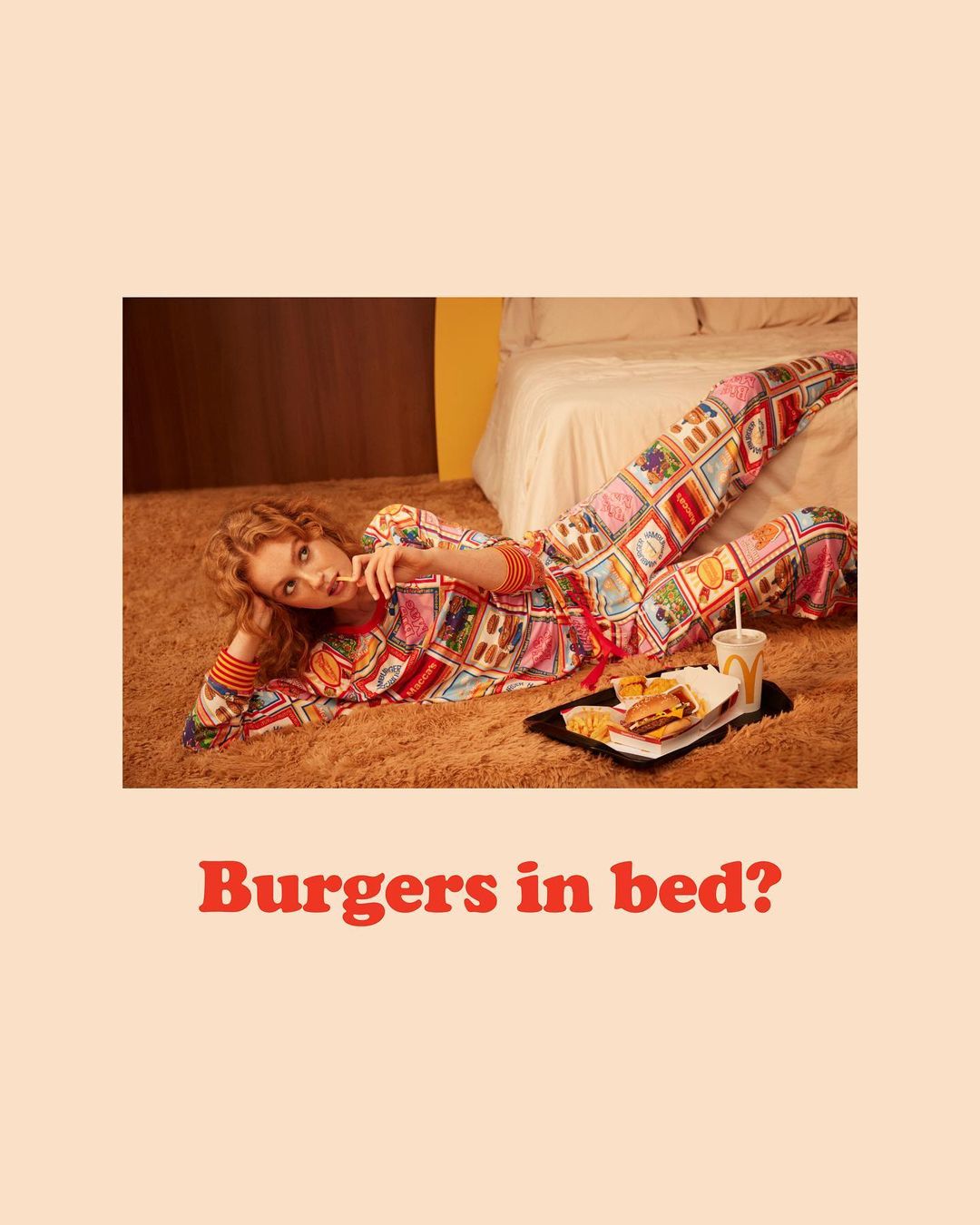 A woman in patterned pajamas lounges on a brown rug next to a tray of fast food, creating a quirky and eye-catching editorial shot.