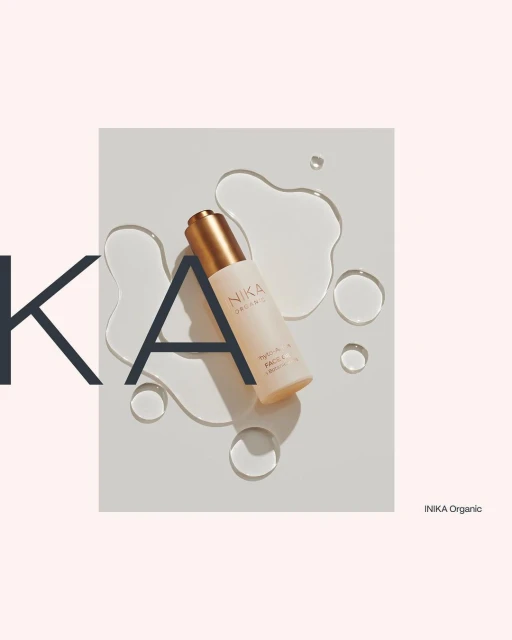 Product shot of NIKA Organic face serum against a white surface with water droplets, accented by oversized typography elements.