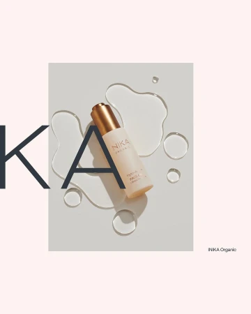 Product shot of NIKA Organic face serum against a white surface with water droplets, accented by oversized typography elements.