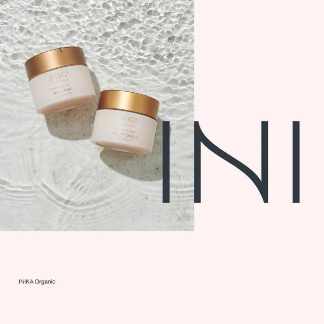 Two Inika Organic skincare jars are displayed against a water-like backdrop, one labeled 'Day Cream' and the other 'Night Cream'.