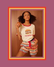 Woman wearing a hamburger graphic t-shirt and patterned shorts holding a burger in a studio portrait by Paper Stone Scissors