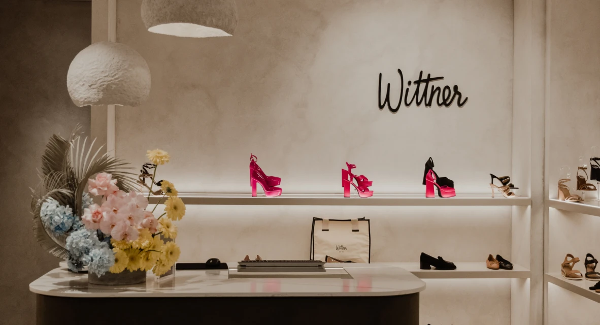 Retail display showcasing pink platform heels on lit shelves against a branded wall with a marble counter and floral arrangement.