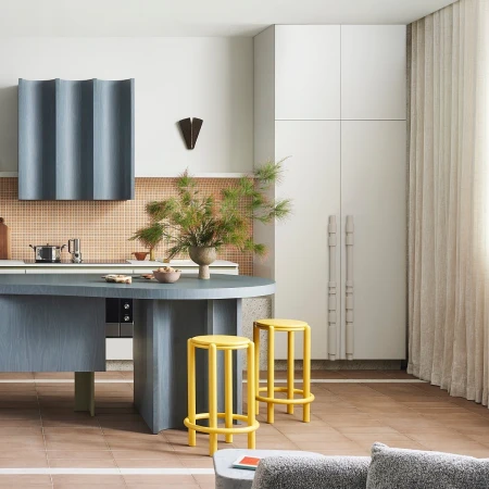 Contemporary kitchen interior featuring a blue island with stools, light peach tiled backsplash, and neutral color palette; indoor daylight.
