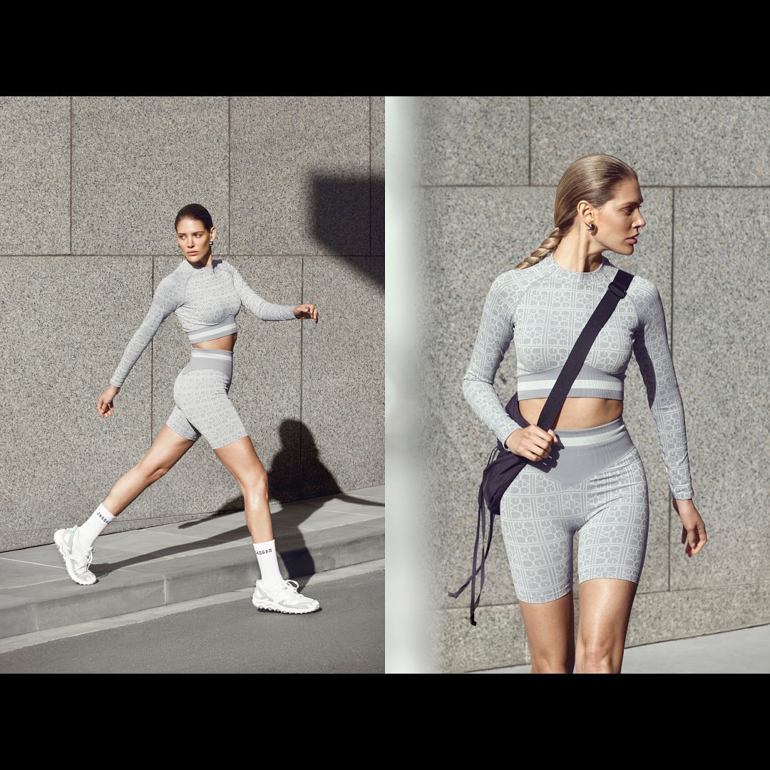 Two angled views of a female adult in grey patterned activewear walking. She wears a matching crop top, shorts, and white sneakers.