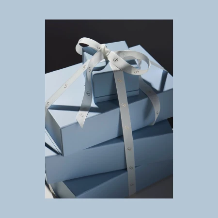 Stacked light blue gift boxes tied with a white ribbon featuring a bow against a dark background