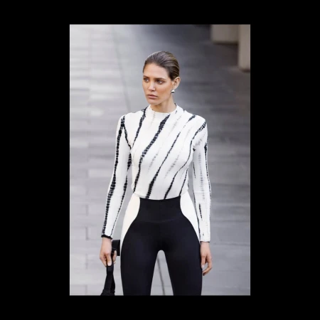 Stylish woman in black and white long-sleeve top and leggings poses on city street with blurred background of grey architecture.