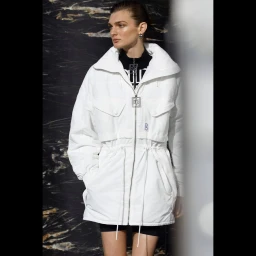 Model wearing a white jacket over a black top against a dark marbled background with a vertical light leak.