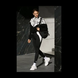 Model in a black and white tie-dye top and leggings walking outdoors past dark marble panels