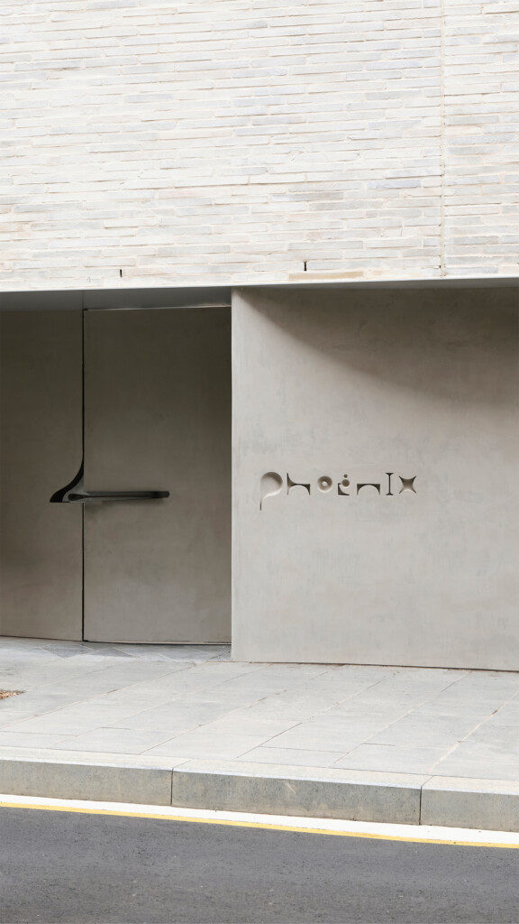 Exterior view of a modern building featuring the word 'Phoenix' subtly engraved on a concrete wall next to a gray door.