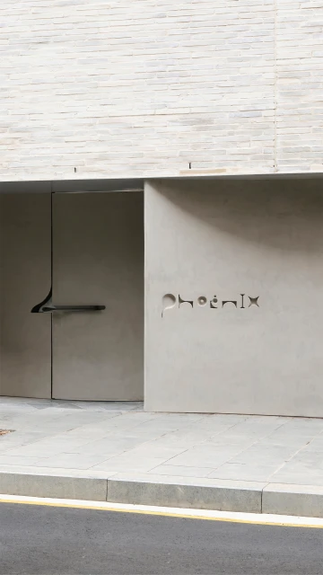 Exterior view of a modern building entrance with a light grey concrete facade and an inscription that reads 'Phoenix'.