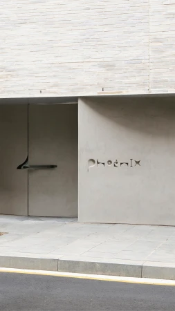 Exterior view of a modern building entrance with a light grey concrete facade and an inscription that reads 'Phoenix'.