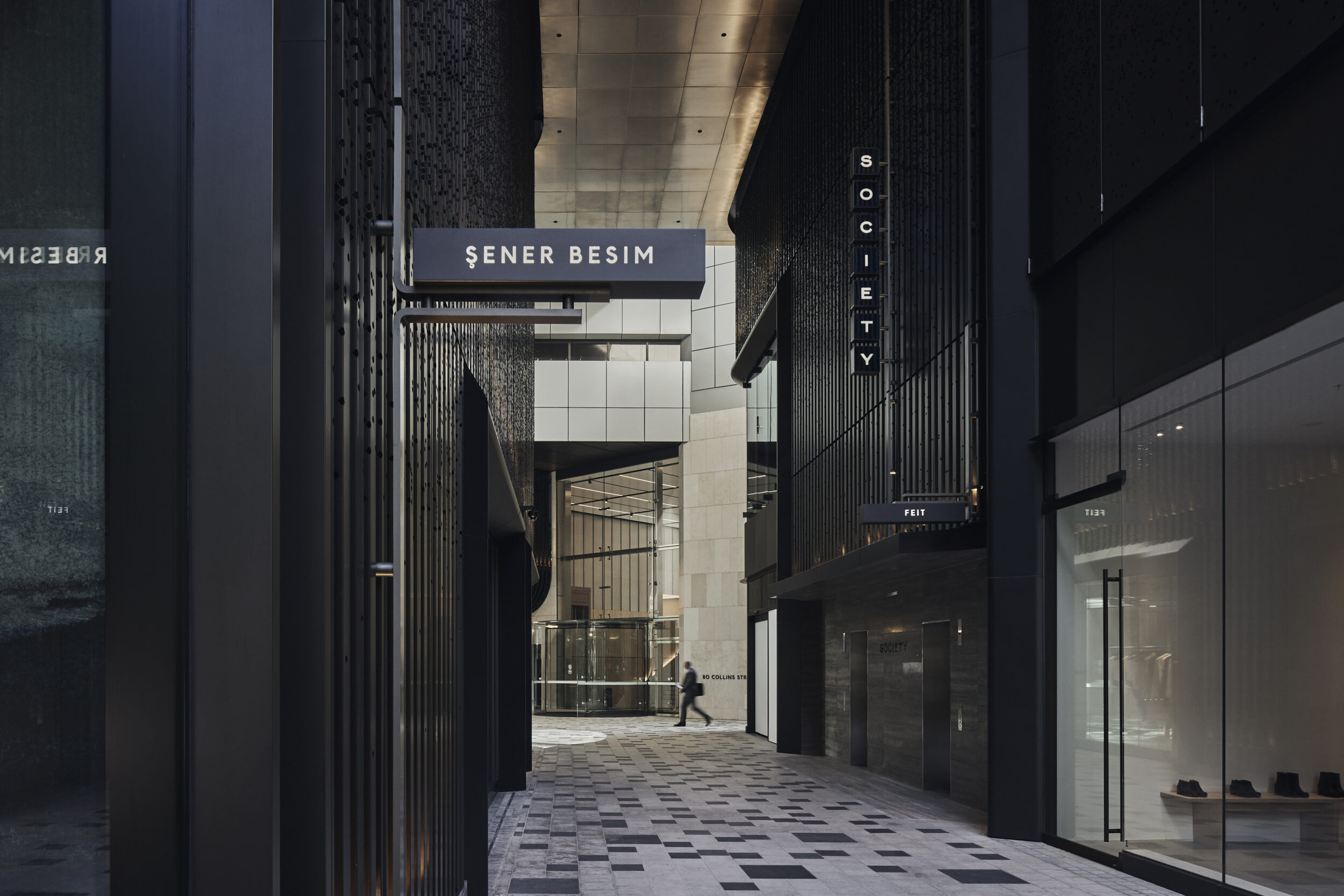 Exterior view of an urban city street with pedestrians, modern architecture, signage, grey stone, and neutral colors, creating a contemporary atmosphere.