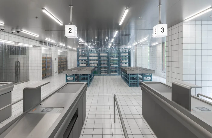 Interior of a modern retail space with white tiled walls, checkout counters in the foreground, and illuminated shelving units.