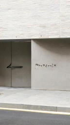 Exterior architectural view of a concrete building facade with inset lettering reading Phoenix above a stone sidewalk.
