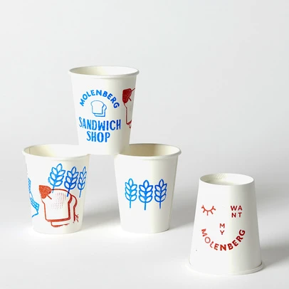 Four white paper cups with blue and red Molenberg Sandwich Shop branding in a studio shot, promoting a playful, vintage aesthetic.