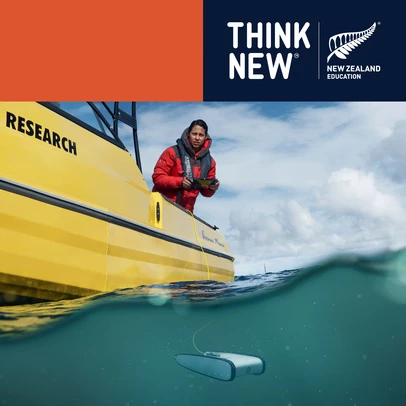 Woman in a red jacket stands on a yellow boat with a black 'RESEARCH' label, monitoring a drone in the ocean under a partly cloudy sky.