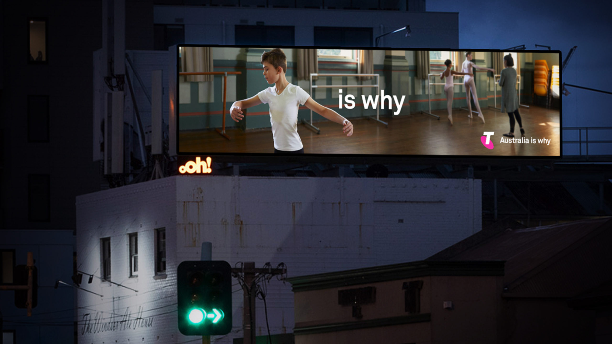 Billboard at night showing a boy ballet dancer on the left and two ballerinas with an instructor on the right; advertisement for Telstra.