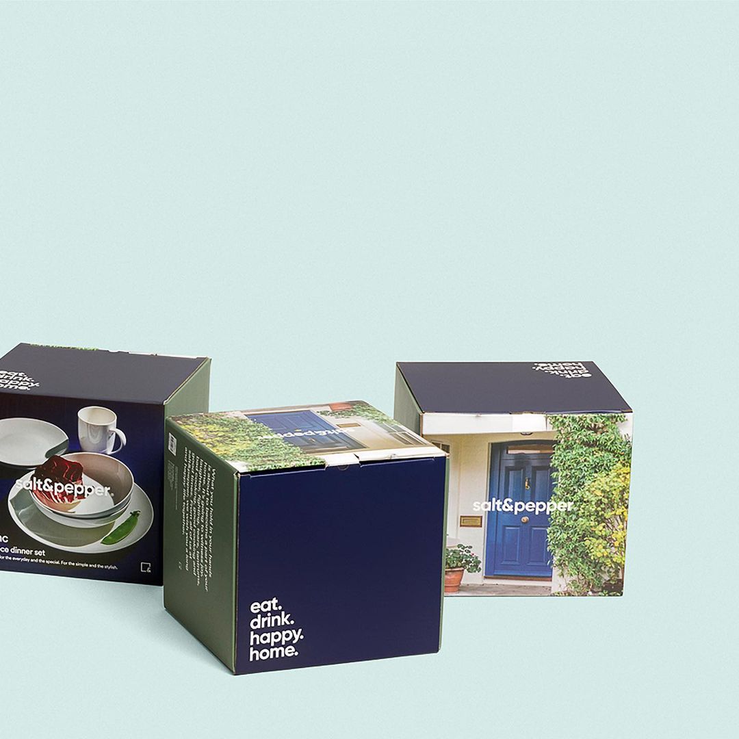 Three Salt & Pepper brand dinnerware set boxes on a light blue background with kitchenware and a home on box designs.
