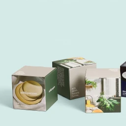 Three branded square product packaging boxes arranged on a pale teal studio surface
