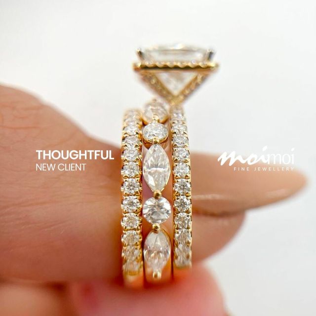 Close-up of a hand holding three gold diamond rings, two eternity bands and one engagement ring, all sparkling against a white background.