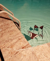 Brown string bikini floating in a clear blue outdoor swimming pool next to a tiled stone edge
