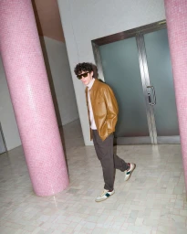 A man wearing a tan leather jacket and sunglasses walks between pink tiled pillars in Sydney.