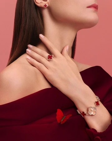 Woman wearing red dress and fine jewelry with four-leaf clover design: earrings, bracelet, and ring. Studio shot on pink background.