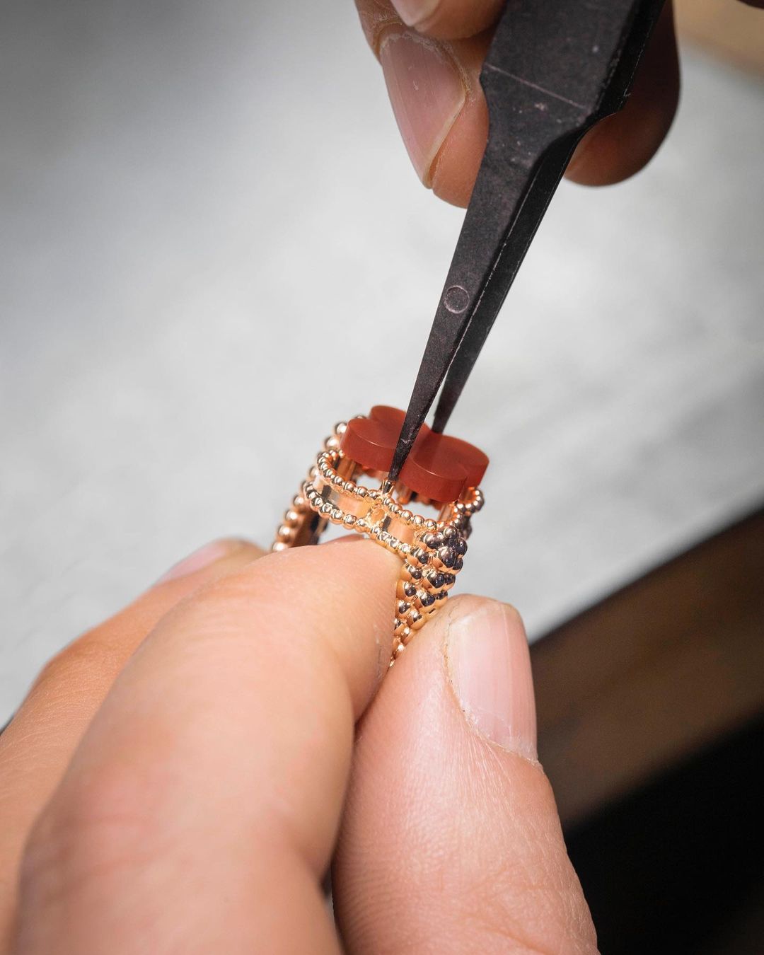 Close-up shot of jeweler's hands using tweezers to set an orange gemstone into a gold bead ring, showcasing fine jewelry making.