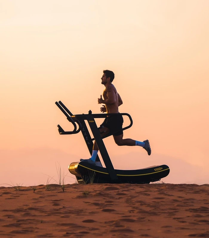 Man running on a curved treadmill set outdoors on a sandy ridge at sunset
