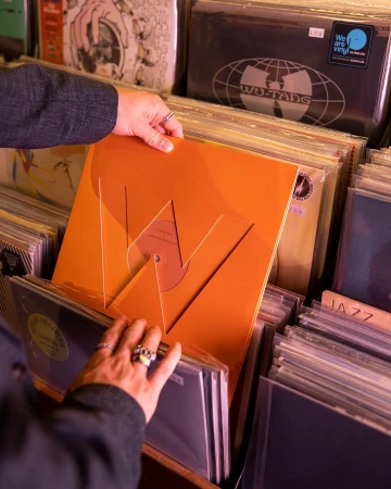 Close-up shot in a music store showing a person's hands flipping through vinyl record albums in a crate, with an orange album in view.