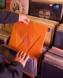 Close-up of hands browsing vinyl records in crates, holding an orange sleeve