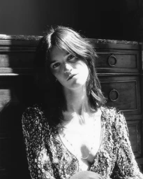 Black and white portrait of a woman with dark hair leaning against a dark wooden chest of drawers in Sydney