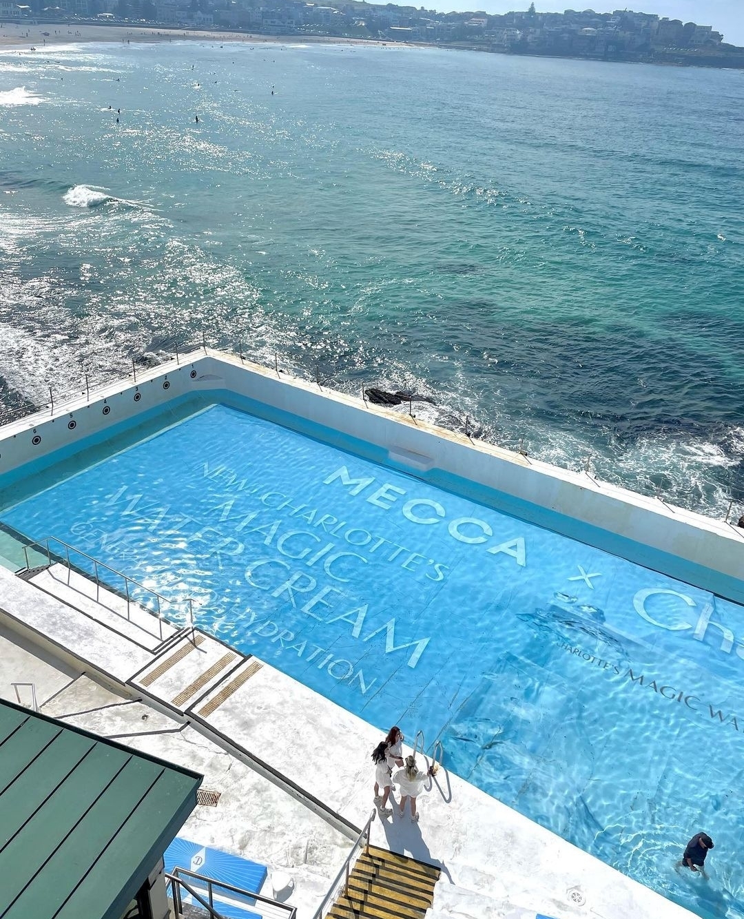 High-angle shot of Bondi Icebergs Pool featuring a MECCA x Charlotte Tilbury advertisement, with beach and ocean backdrop.