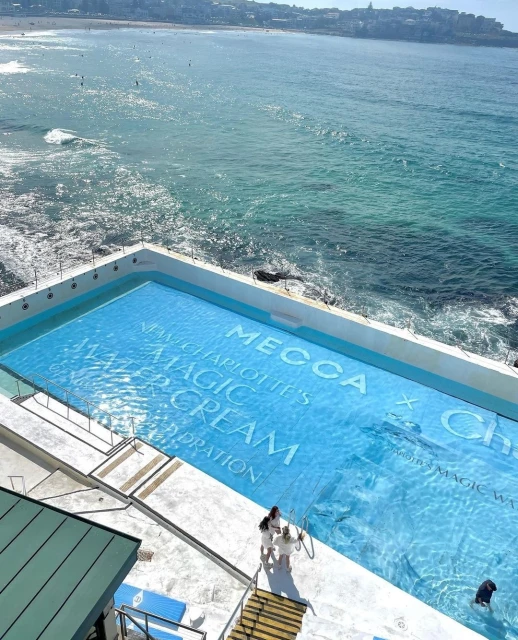 High-angle shot of Bondi Icebergs Pool featuring a MECCA x Charlotte Tilbury advertisement, with beach and ocean backdrop.