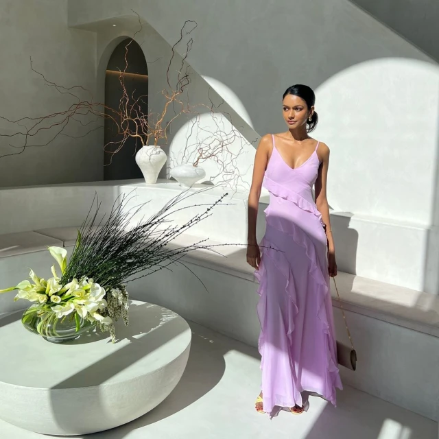 Woman in a lavender gown stands in a brightly lit interior with modern architectural details and a white flower arrangement.
