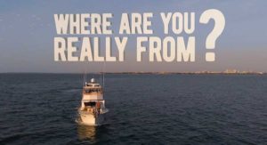 A white boat moves across the water with text overlay, “Where are you really from?” against a blue sky and horizon.