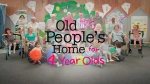 A large group of elderly adults and young children gathered together in a brightly decorated room for a shared community activity.