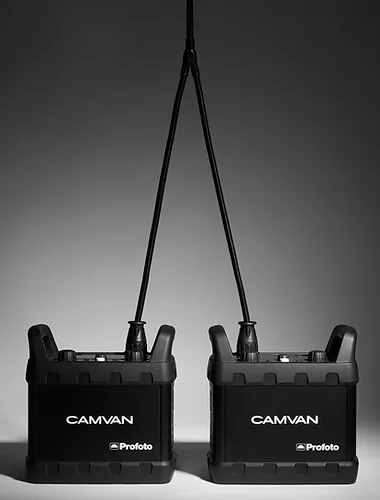 Two black Profoto CamVan battery packs are positioned side-by-side, each connected by a black cable against a gradient grey background.