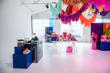 Colorful product display tables inside a bright studio with hanging metallic tinsel garlands and mirrored panels.