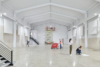 Wide interior view of a large white warehouse with workers operating a scissor lift and floor cleaning equipment