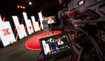 Professional broadcast camera capturing a speaker on a red stage with glowing panels in Sydney by Pix.