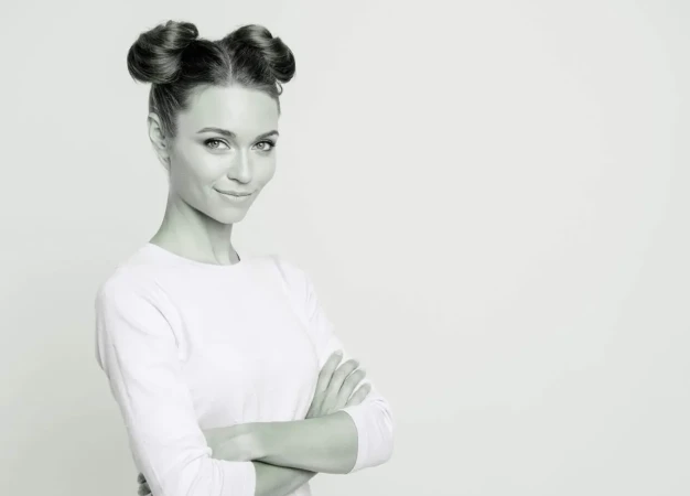 Portrait of a woman with double hair buns and folded arms against a white background by Lime Agency