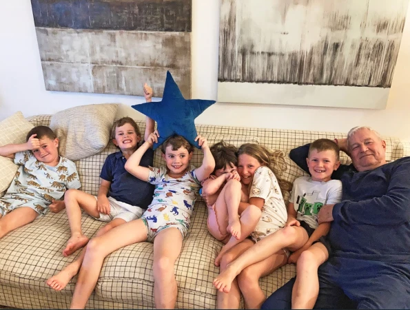 Group of children and an elderly man sitting on a patterned sofa holding a blue star pillow in Melbourne