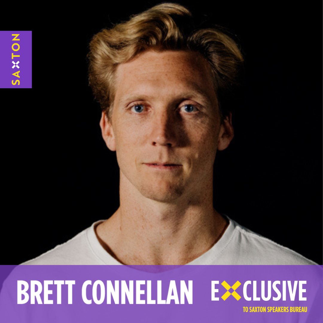 Portrait of a blond-haired man in a white t-shirt against a dark backdrop. Saxton Speakers Bureau logo in frame. Promotional headshot.