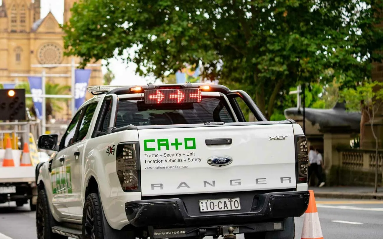 Ford Ranger pickup truck with a lighted arrow board and CA+O company graphics, parked on a city street near trees and a cathedral.